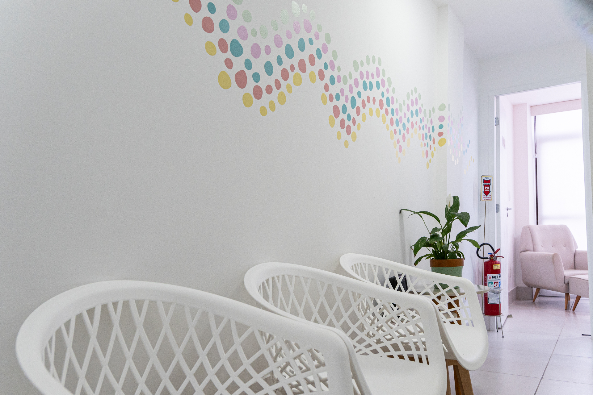 Recepção do Espaço CoReS com parede decorada com bolinhas coloridas e poltronas brancas.
