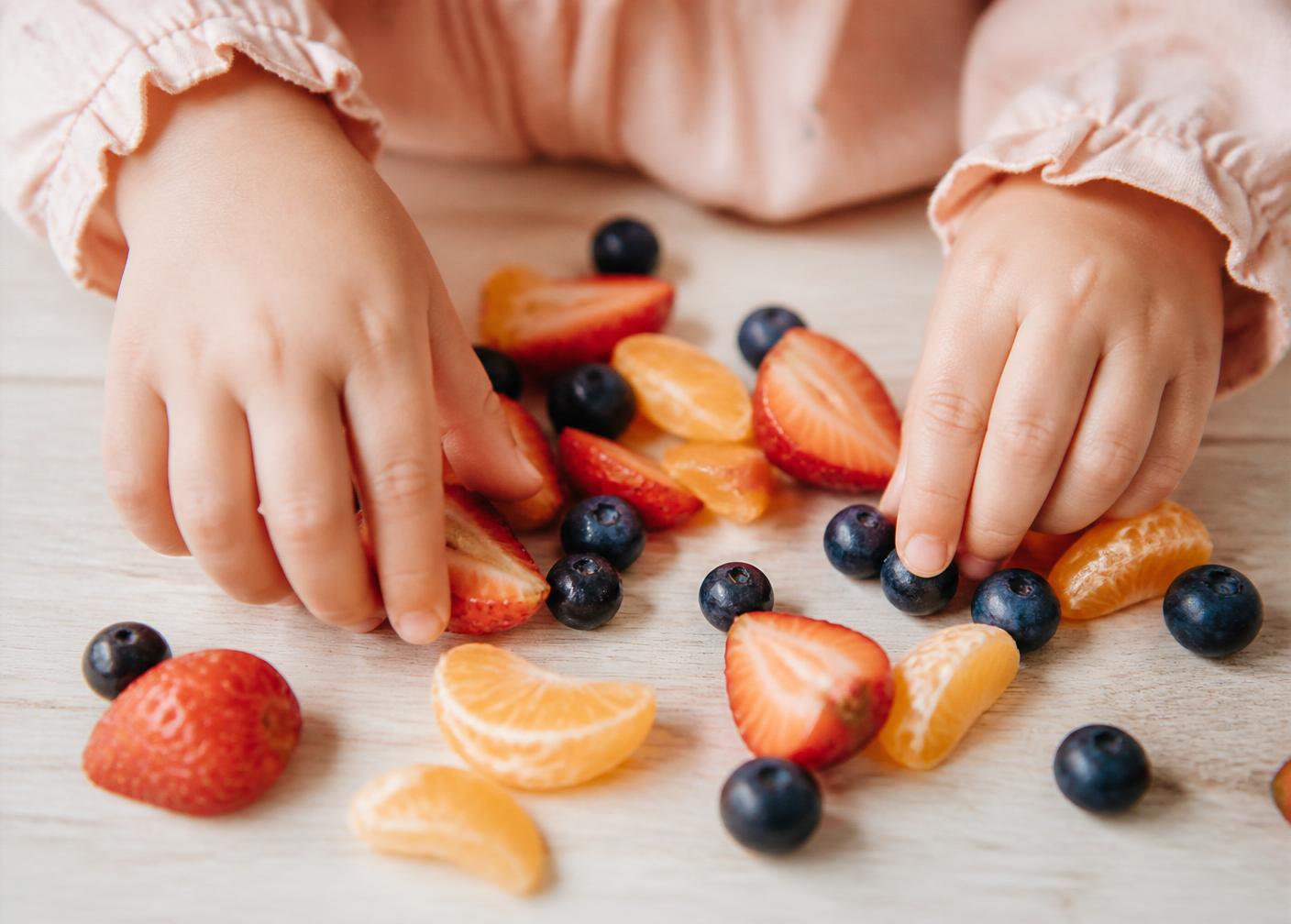 Mãos infantis explorando frutas coloridas em atividade sensorial