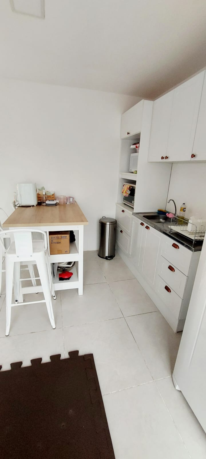 Bancada da cozinha terapêutica com armários brancos, pia e banquetas.